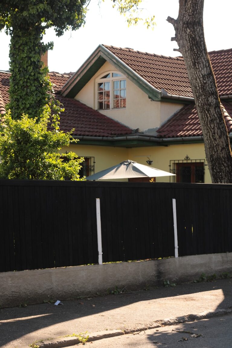 a house behind a fence with a tree in front of it
