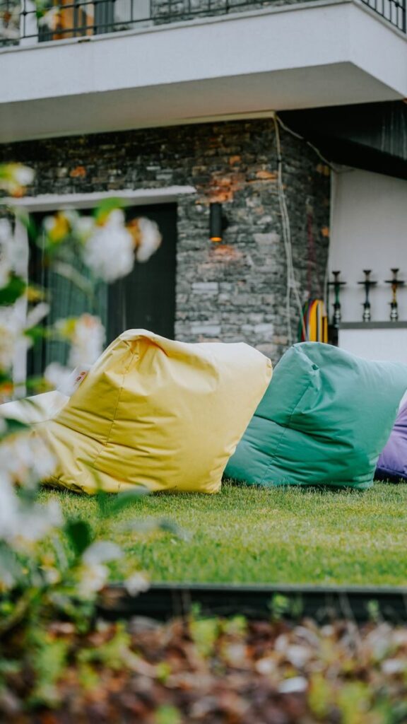 Geef je tuin een warme uitstraling met douglas hout Vibrant bean bags on a garden lawn in front of a modern house with stone walls.